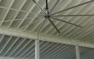 Stalla con mucche, tetto a travi e ventilatore industriale.