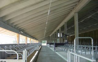 Interno di una stalla con struttura metallica e tetto in cemento.