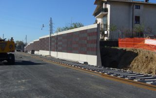 Dettaglio di una barriera fonoassorbente "Paver Sound" con superficie a rilievo in cemento e inserti colorati.