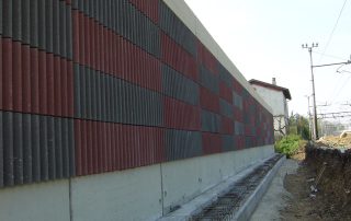 Dettaglio di una barriera fonoassorbente "Paver Sound" con superficie a rilievo in cemento e inserti colorati.