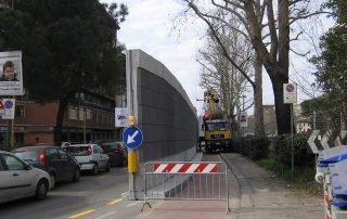 Installazione di una barriera fonoassorbente in cemento lungo una strada urbana.