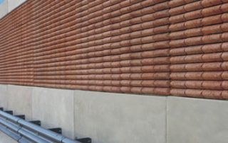 Barriera fonoassorbente lungo una strada, caratterizzata da una texture in rilievo con elementi in laterizio e una base in cemento.