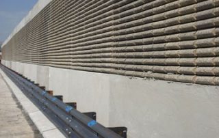 Barriera fonoassorbente lungo una strada, caratterizzata da una texture in rilievo con elementi in laterizio e una base in cemento.