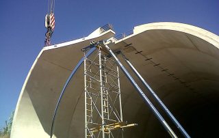 Montaggio di una galleria artificiale in cemento armato con l'ausilio di una gru e impalcature di sostegno.