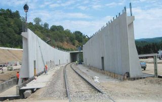 Galleria artificiale prefabbricata in cemento armato in fase di costruzione sopra una linea ferroviaria.
