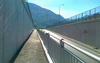 Strada a doppia corsia in trincea con pareti in cemento armato e barriere di sicurezza in metallo.