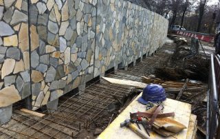 Muro di sostegno prefabbricato in calcestruzzo con finitura in pietra naturale, in fase di installazione.