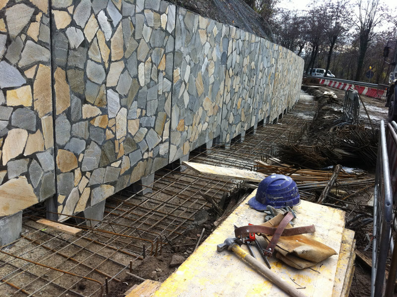 Muro di sostegno prefabbricato in calcestruzzo con finitura in pietra naturale, in fase di installazione.
