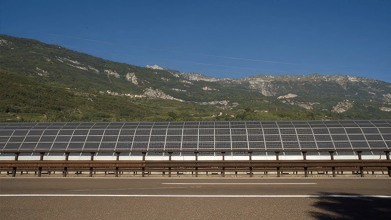 "Barriera fonoassorbente con pannelli fotovoltaici integrati lungo un'autostrada.