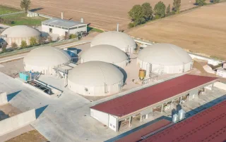 Veduta aerea di un impianto di biogas con più biodigestori coperti, aree di stoccaggio per biomasse e strutture di supporto.