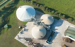 Veduta aerea di un impianto di biogas con tre biodigestori di forma cilindrica coperti.