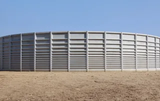 Vasca agricola circolare in metallo con struttura rinforzata a pannelli. L'installazione si trova in un'area aperta con terreno asciutto.