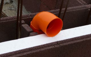 Cantiere con blocchi BioPLUS® in fase di costruzione. Un raccordo arancione per tubazioni è posizionato tra i blocchi.