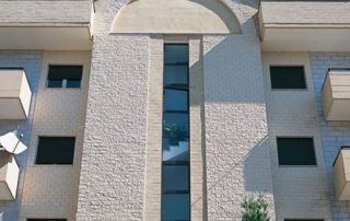 Facciata di un edificio residenziale con rivestimento in mattoni chiari e dettagli architettonici geometrici.