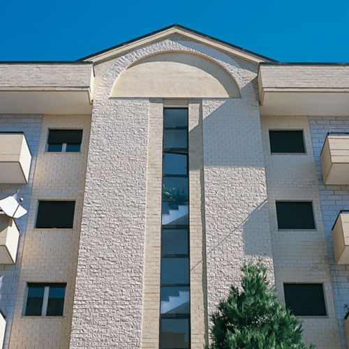 Facciata di un edificio residenziale con rivestimento in mattoni chiari e dettagli architettonici geometrici.