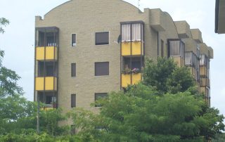 Edificio residenziale con facciata in blocchi di cemento dall'aspetto materico e balconi con parapetti gialli.