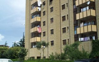 Edificio residenziale con facciata in blocchi di cemento dall'aspetto materico e balconi con parapetti gialli.