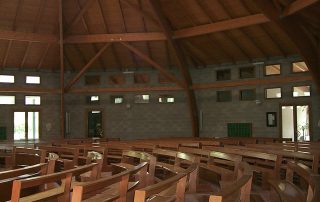 Interno di una chiesa con struttura in legno a vista e pareti in blocchi di cemento.