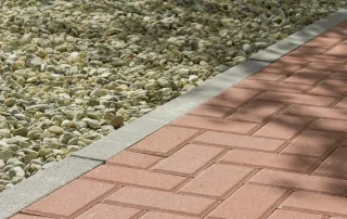 ordolo in cemento delimitante un vialetto pavimentato con autobloccanti rossi e un'area con ghiaia.