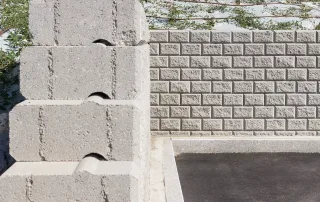 Dettaglio di un muro di contenimento in blocchi Muricciolo grigi, con vista frontale e laterale che evidenzia l'incastro tra gli elementi modulari.