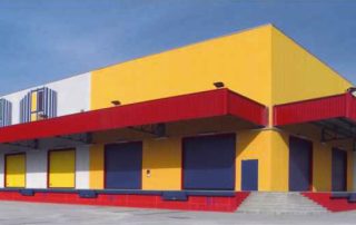 Magazzino industriale con facciata colorata in pannelli prefabbricati gialli, rossi e blu.