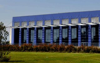 Edificio industriale moderno con facciata in pannelli prefabbricati blu e ampie vetrate.