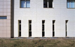 Facciata di un edificio realizzata con Lecablocco bianco, con finestre verticali strette e finestre orizzontali più ampie.