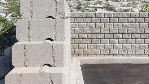 Dettaglio di un muro di contenimento in blocchi Muricciolo grigi, con vista frontale e laterale che evidenzia l'incastro tra gli elementi modulari.
