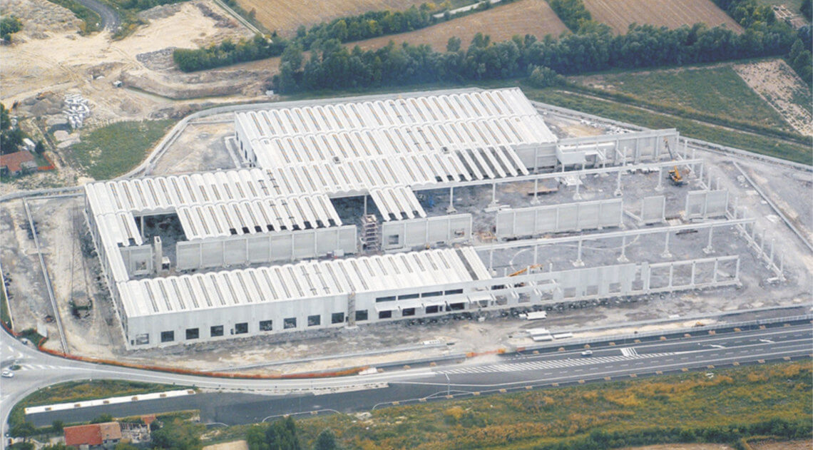 Vista aerea di un grande edificio industriale in costruzione, con una struttura modulare in cemento e coperture parzialmente installate.