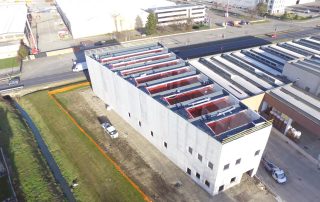 Capannone prefabbricato in costruzione ripreso dall’alto, con struttura in cemento armato e copertura ancora in fase di installazione.