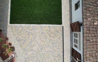 Pavimentazione in autobloccanti di pietra dai toni caldi davanti a una cascina nell’Oltrepò Pavese con pareti in pietra e vegetazione rampicante.