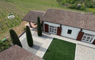 Pavimentazione in autobloccanti di pietra dai toni caldi davanti a una cascina nell’Oltrepò Pavese con pareti in pietra e vegetazione rampicante.