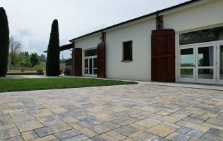 Pavimentazione in autobloccanti di pietra dai toni caldi davanti a una cascina nell’Oltrepò Pavese con pareti in pietra e vegetazione rampicante.