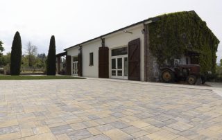 Pavimentazione in autobloccanti di pietra dai toni caldi davanti a una cascina nell’Oltrepò Pavese con pareti in pietra e vegetazione rampicante.
