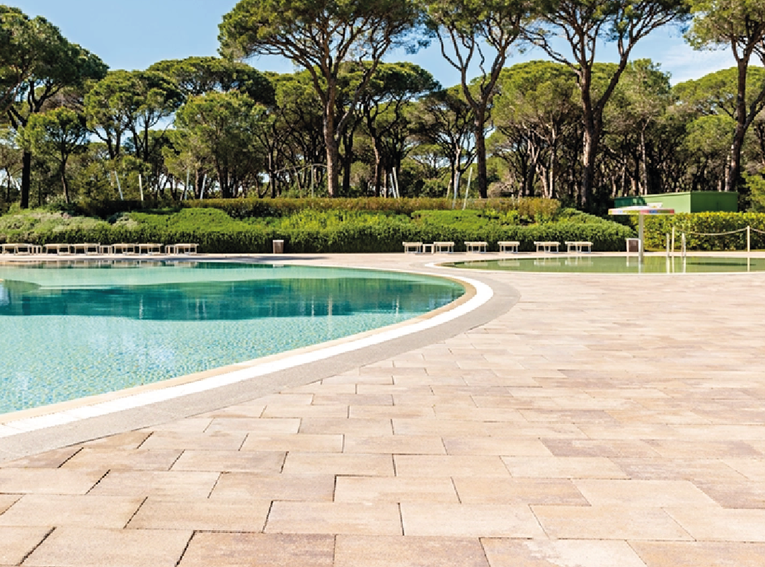 Pavimentazione in masselli autobloccanti attorno a due piscine, una più ampia e una più piccola con area giochi d'acqua.