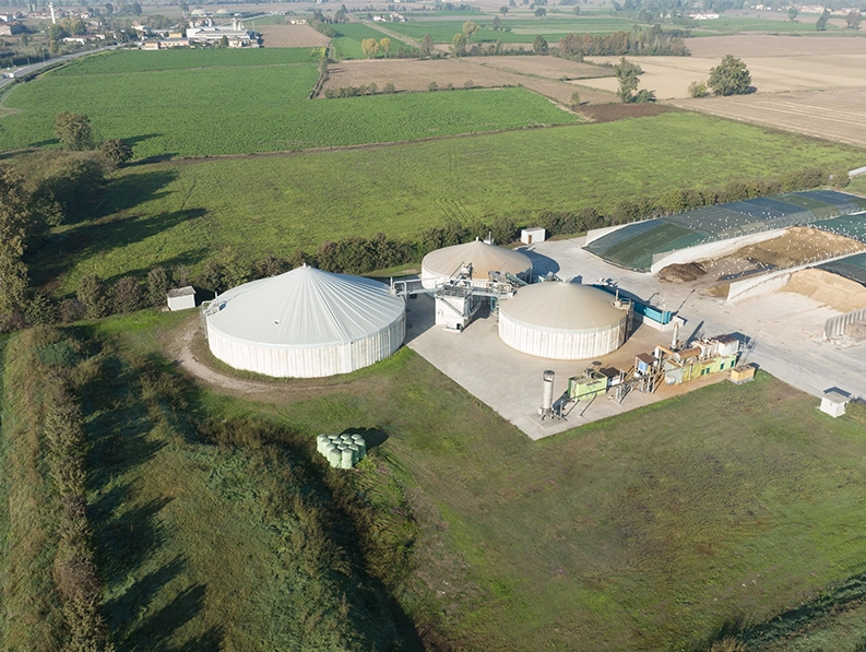 Veduta aerea di un impianto di biogas con tre biodigestori di forma cilindrica coperti.