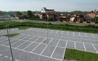 Pavimentazione in blocchetti di pietra grigia in un parcheggio con segnaletica bianca.