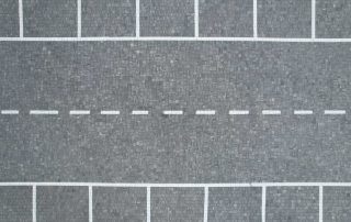 Pavimentazione in blocchetti di pietra grigia in un parcheggio con segnaletica bianca.