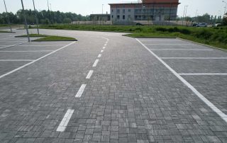 Pavimentazione in blocchetti di pietra grigia in un parcheggio con segnaletica bianca.