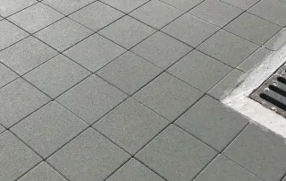 Pavimentazione in cemento modello "Aurelia", con superficie liscia e formato quadrato con fughe regolari, di colore grigio scuro.