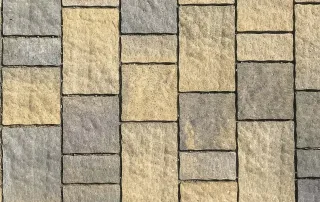 Pavimentazione in cemento con blocchi rettangolari di colore giallo e grigio disposti in modo alternato.