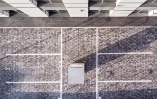 Parcheggio pavimentato con blocchi di cemento grigi, suddiviso da linee bianche che delimitano gli spazi per le auto.