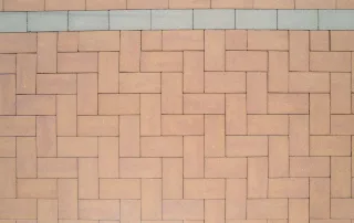 Sentiero pavimentato con blocchi in cemento color mattone e bordi chiari.