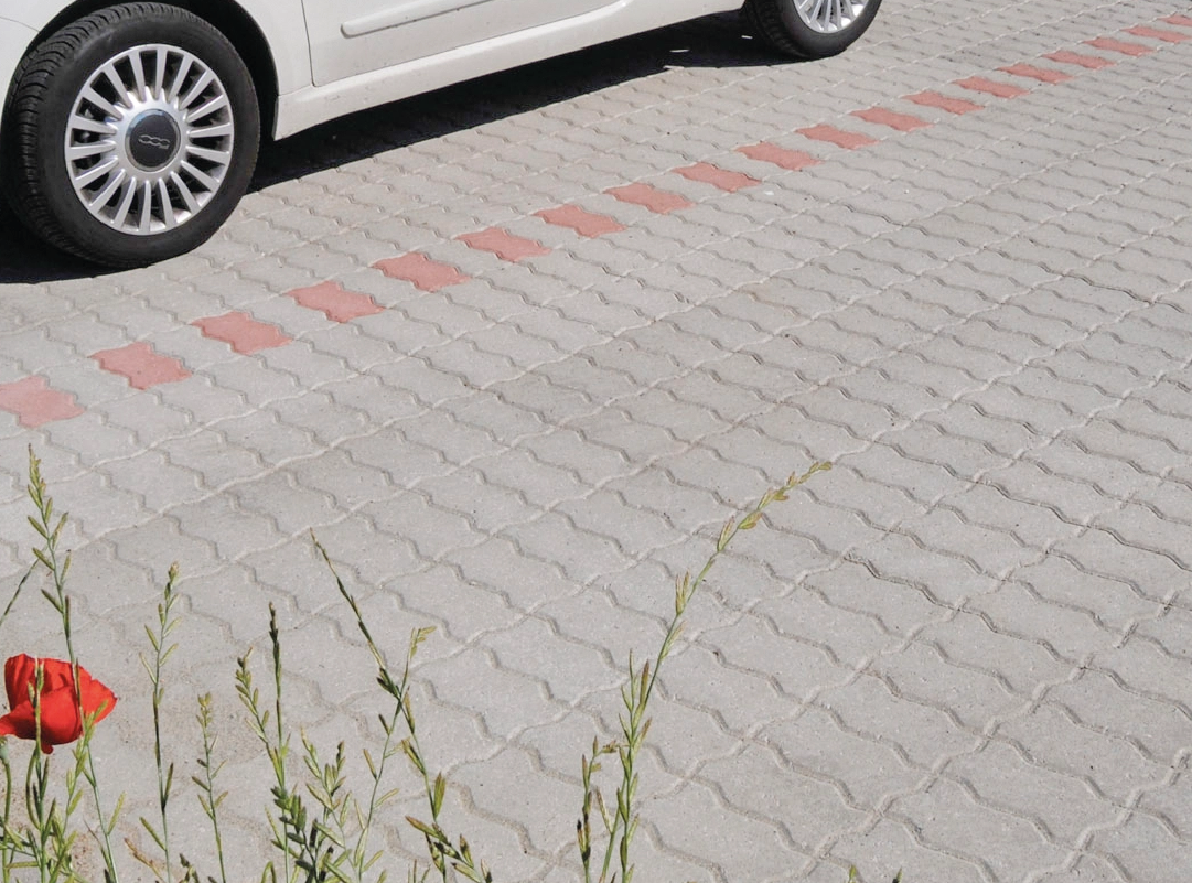 Parcheggio pavimentato con autobloccanti in calcestruzzo grigio a incastro, con una fascia di segnalazione in blocchi rossi.