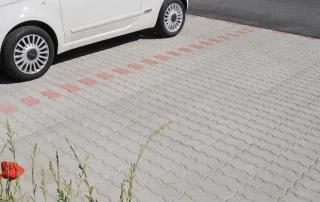 Parcheggio pavimentato con autobloccanti in calcestruzzo grigio a incastro, con una fascia di segnalazione in blocchi rossi.