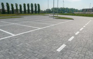 Ampio parcheggio pavimentato in blocchi di pietra grigia con segnaletica bianca per i posti auto.