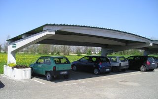 Struttura prefabbricata in cemento con copertura ondulata, utilizzata come parcheggio coperto.