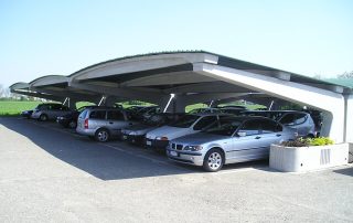 Struttura prefabbricata in cemento con copertura ondulata, utilizzata come parcheggio coperto.