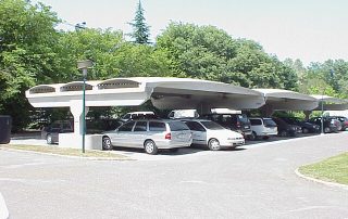 Struttura prefabbricata in cemento con copertura ondulata, utilizzata come parcheggio coperto.