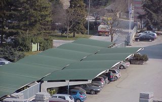 Parcheggio coperto con struttura prefabbricata in cemento e tettoia ondulata in lamiera verde.